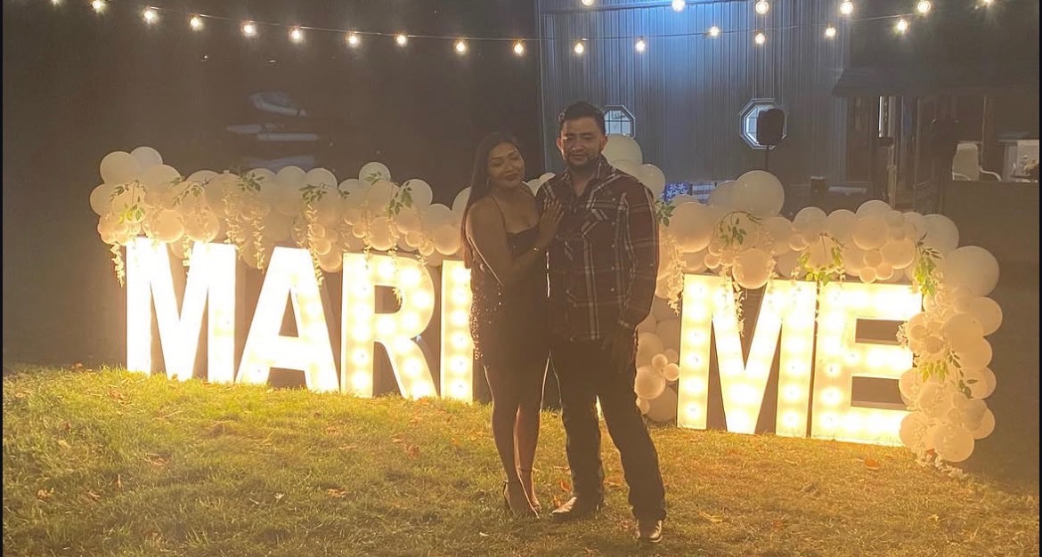 Couple posing in front of illuminated Marry Me marquee letters at an NBT event