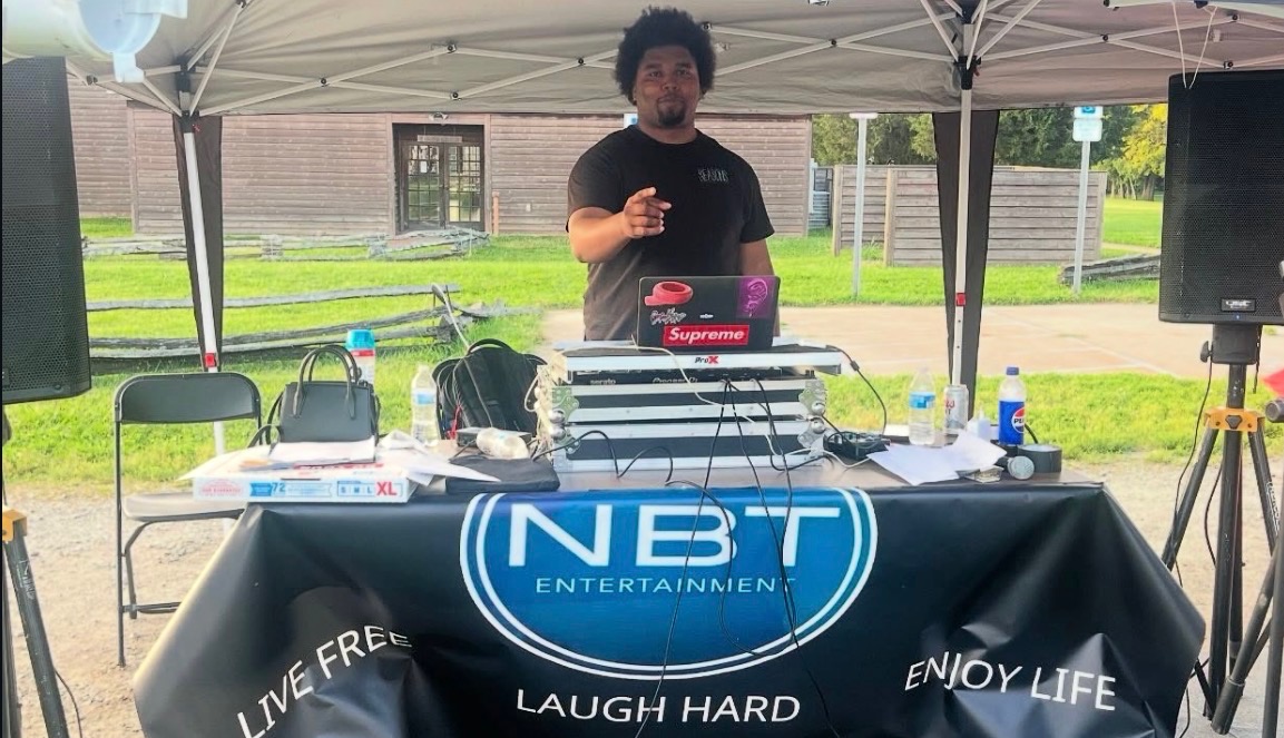 NBT Entertainment DJ hosting an outdoor tent event with branded banner