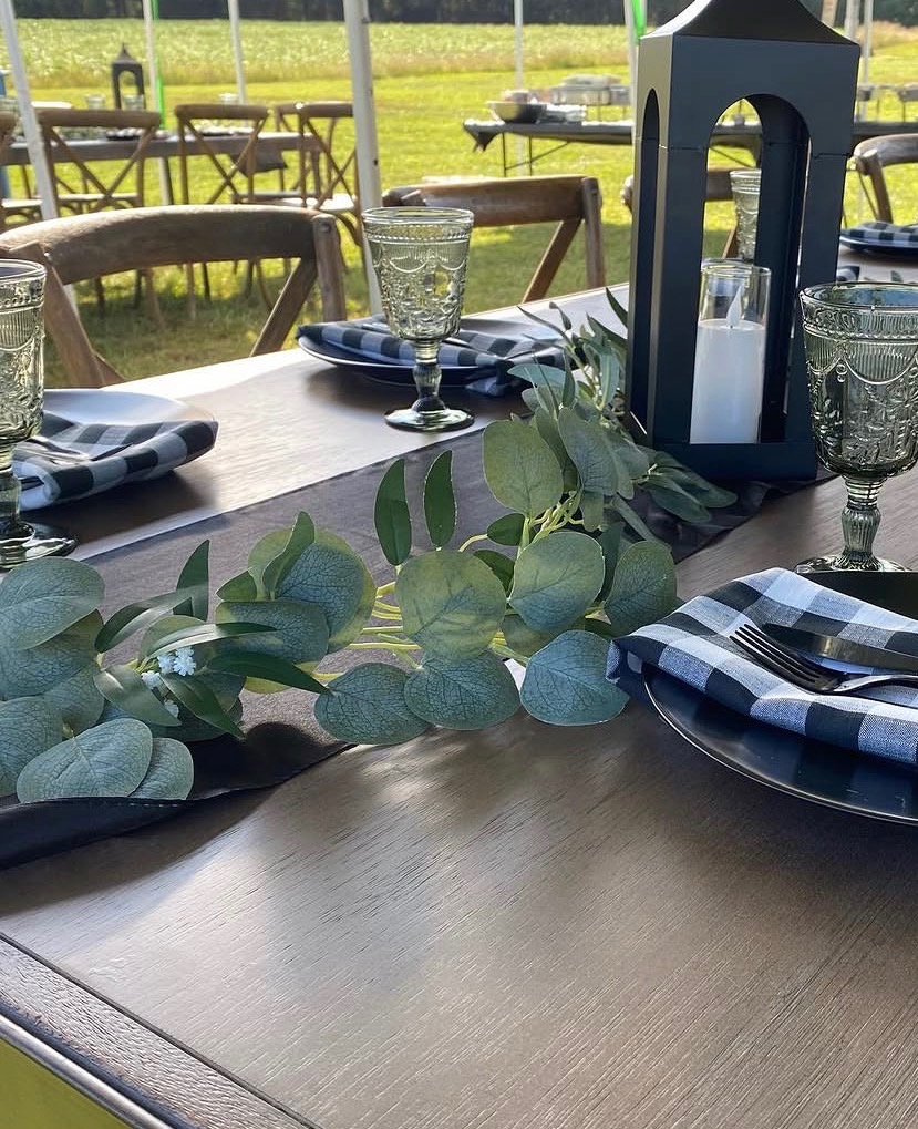 Rustic outdoor tent reception table with lanterns, goblets and greenery centerpiece