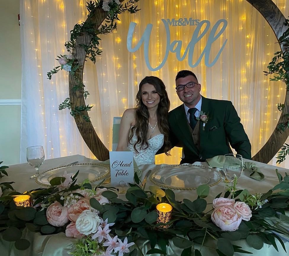 Bride and groom at Mr and Mrs Wall sweetheart table with floral centerpiece