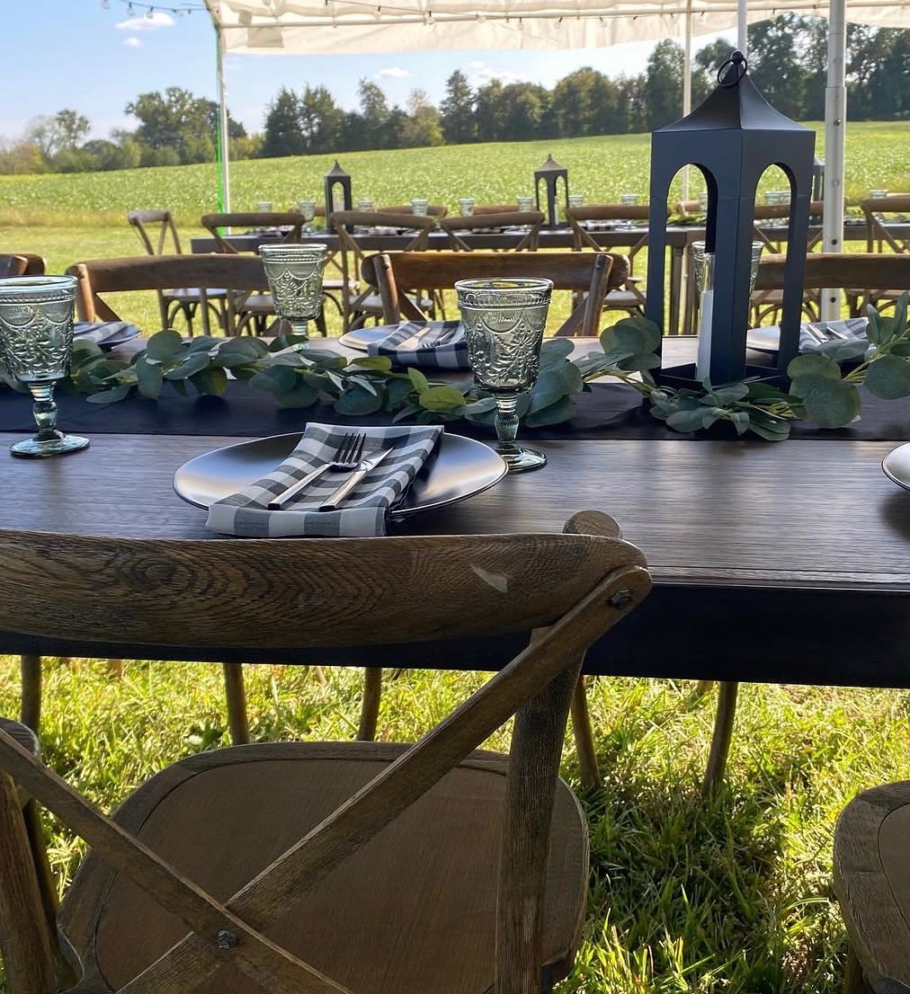 Outdoor farm-style tented reception dining setup with lanterns and greenery